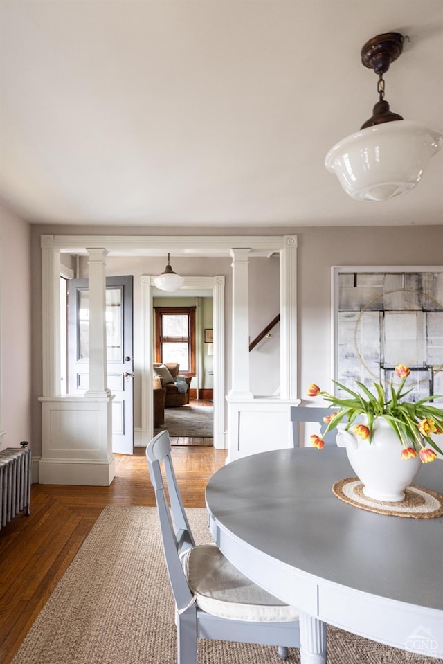 dining area featuring decorative columns, wood finished floors, and radiator heating unit