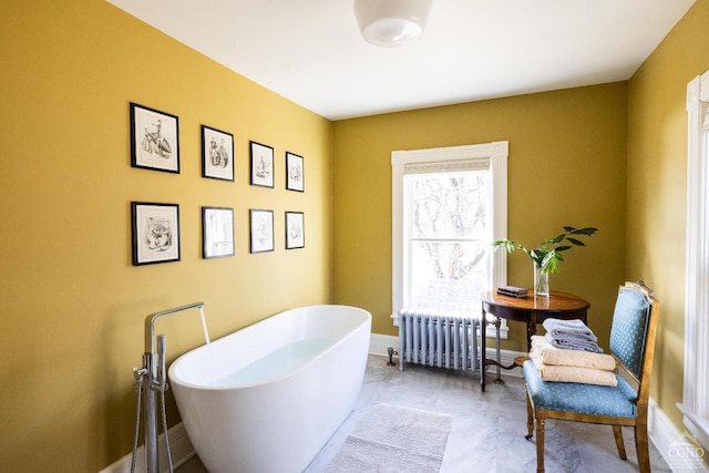 full bathroom with radiator, a freestanding bath, and baseboards