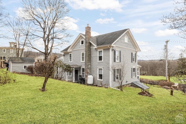 back of property featuring a yard, an outdoor structure, and a chimney