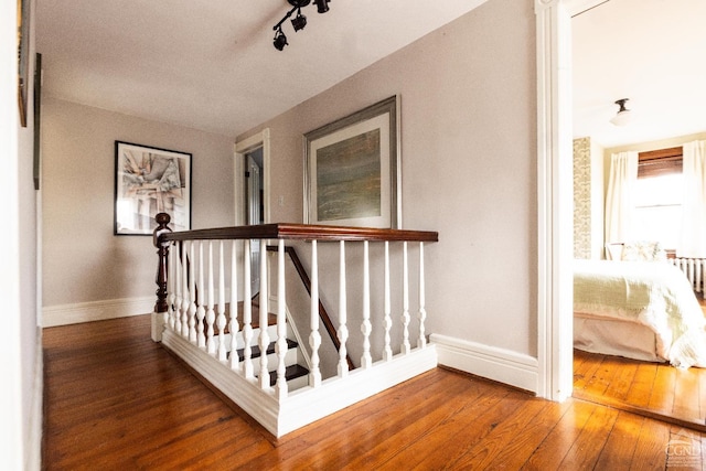 stairs with hardwood / wood-style floors, rail lighting, and baseboards