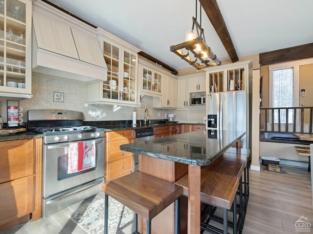 kitchen featuring a breakfast bar area, stainless steel appliances, hanging light fixtures, custom exhaust hood, and glass insert cabinets