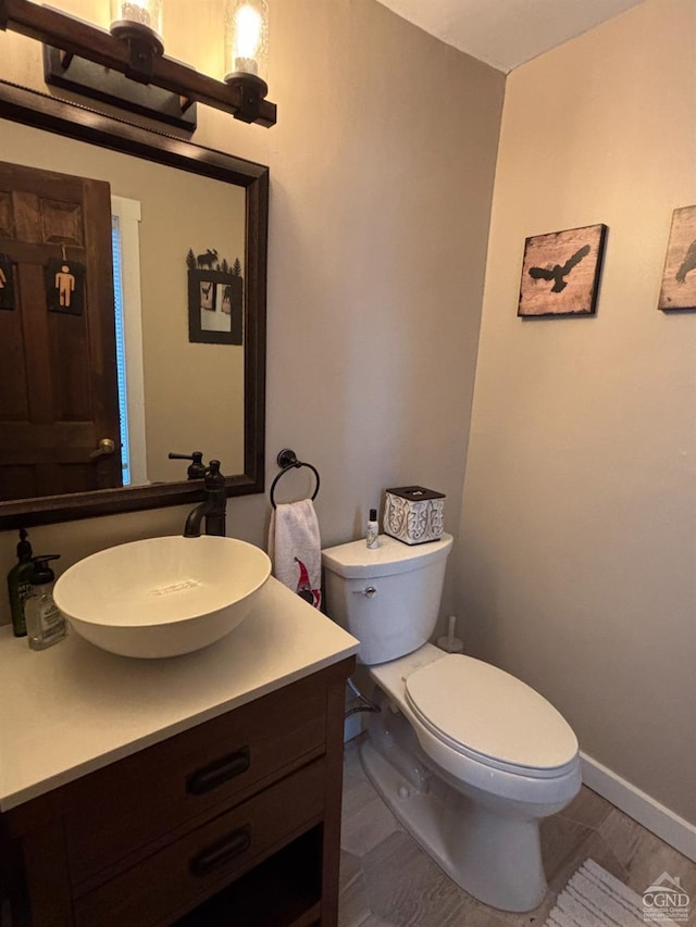 half bath featuring baseboards, vanity, and toilet