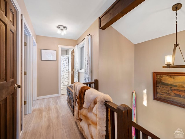 hallway with lofted ceiling with beams, light wood finished floors, and baseboards