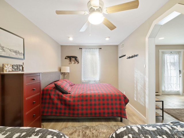 bedroom with light wood-type flooring, ceiling fan, visible vents, and a baseboard radiator