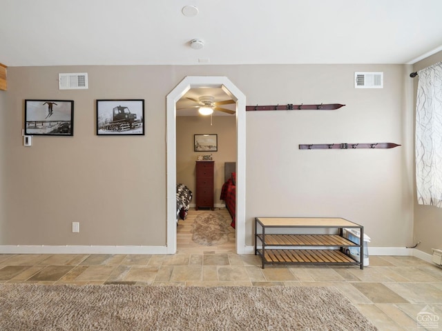 hall featuring stone finish floor, visible vents, and baseboards