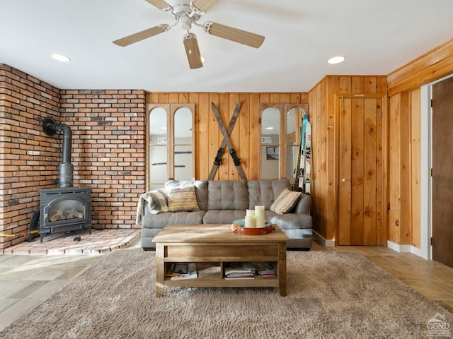 living room with a ceiling fan, stone tile flooring, a wood stove, and wooden walls