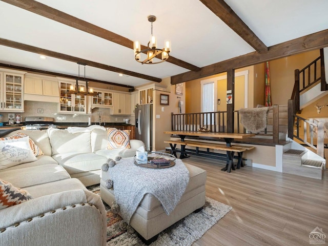 living room with beam ceiling, light wood-style flooring, stairway, an inviting chandelier, and baseboards