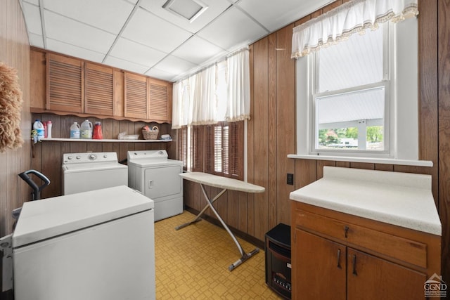 laundry room with wooden walls, light floors, cabinet space, and washing machine and clothes dryer