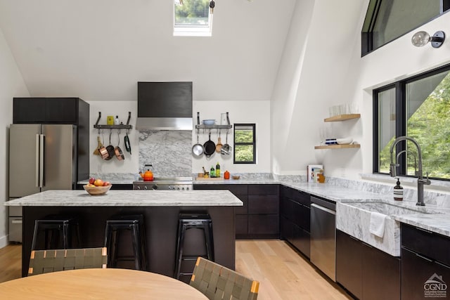 kitchen featuring appliances with stainless steel finishes, light wood-type flooring, light stone counters, and wall chimney exhaust hood