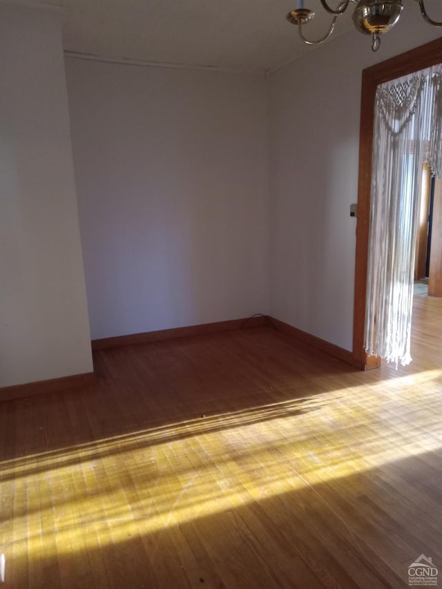 empty room with wood-type flooring and an inviting chandelier