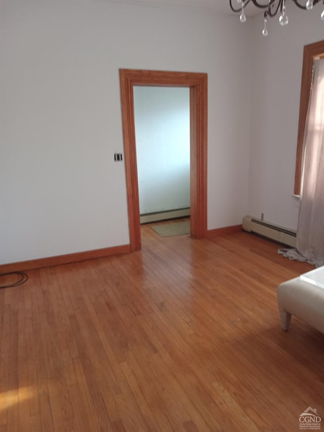 unfurnished room with a notable chandelier, light wood-type flooring, and a baseboard radiator