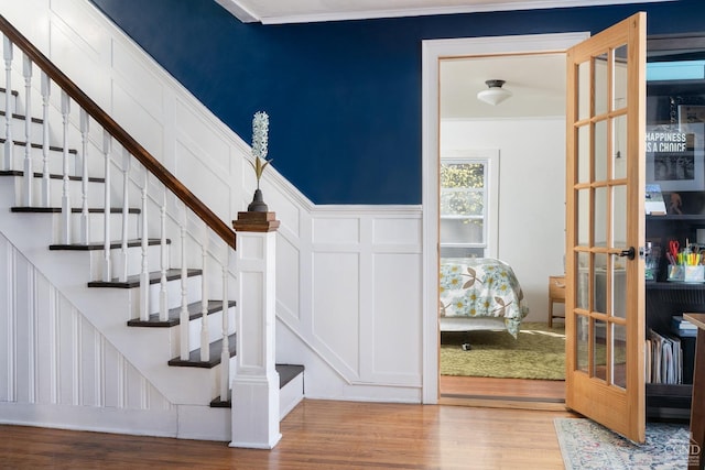 stairway featuring wood finished floors, french doors, and a decorative wall