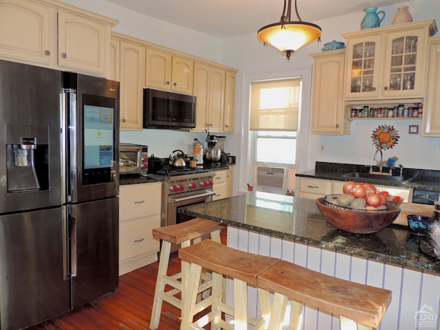 kitchen with a kitchen breakfast bar, stainless steel appliances, decorative light fixtures, sink, and dark stone countertops