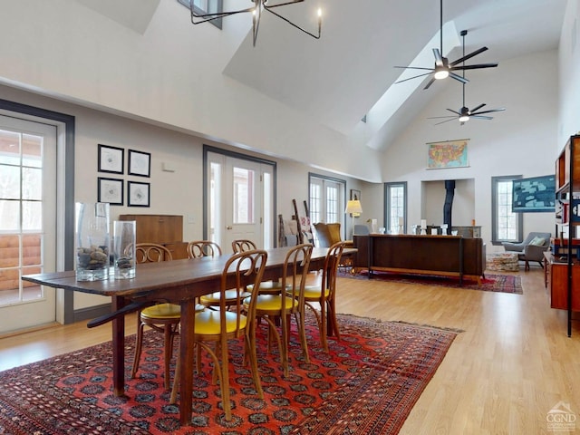 dining area with high vaulted ceiling, ceiling fan, and light wood finished floors