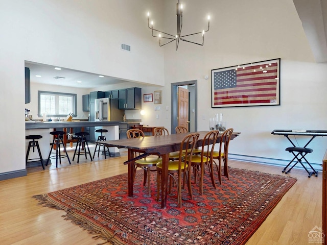 dining area featuring light wood finished floors, baseboards, visible vents, an inviting chandelier, and a high ceiling