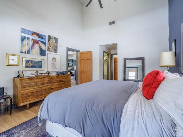 bedroom with visible vents, ceiling fan, a towering ceiling, and wood finished floors