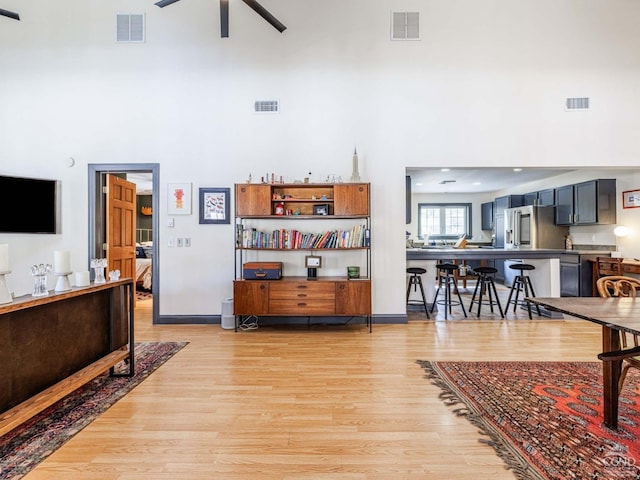 living room featuring a towering ceiling, light wood finished floors, and visible vents