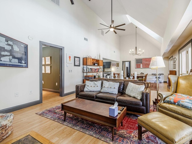 living area featuring high vaulted ceiling, light wood-style flooring, ceiling fan with notable chandelier, visible vents, and baseboards