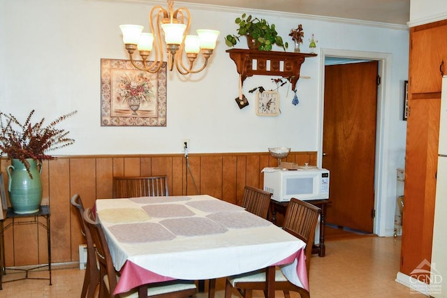 dining space featuring crown molding, wooden walls, and an inviting chandelier