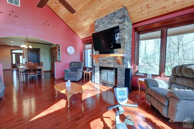 living room with wood ceiling, ceiling fan with notable chandelier, high vaulted ceiling, hardwood / wood-style floors, and a stone fireplace