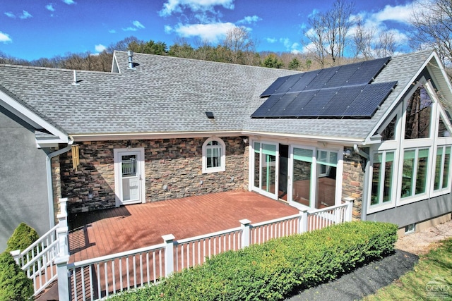 back of property with a wooden deck and solar panels