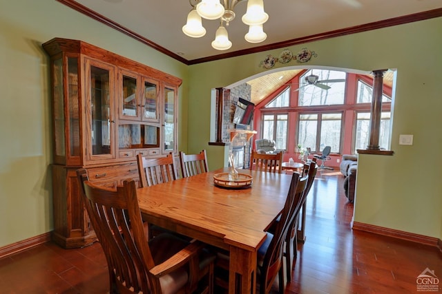 dining space featuring ceiling fan with notable chandelier, a stone fireplace, dark hardwood / wood-style flooring, and ornamental molding