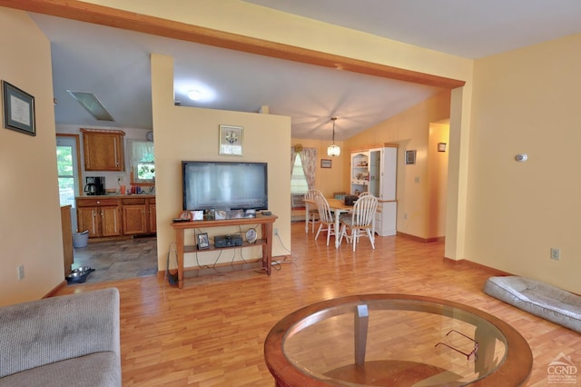 living area with light wood-style floors, lofted ceiling, a healthy amount of sunlight, and baseboards