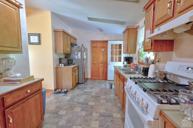 kitchen with stone finish floor, stainless steel appliances, light countertops, under cabinet range hood, and a sink