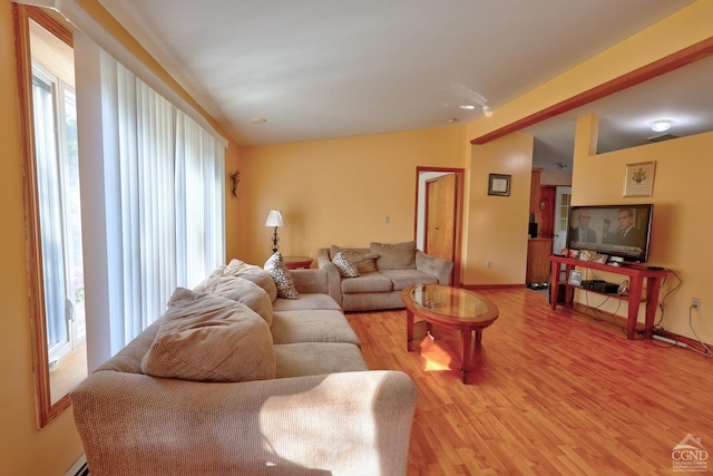 living room with vaulted ceiling, a baseboard heating unit, light wood finished floors, and baseboards