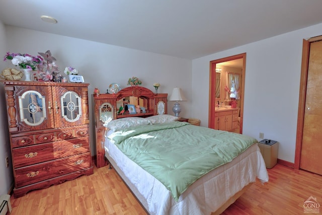 bedroom with light wood finished floors, baseboards, baseboard heating, and connected bathroom