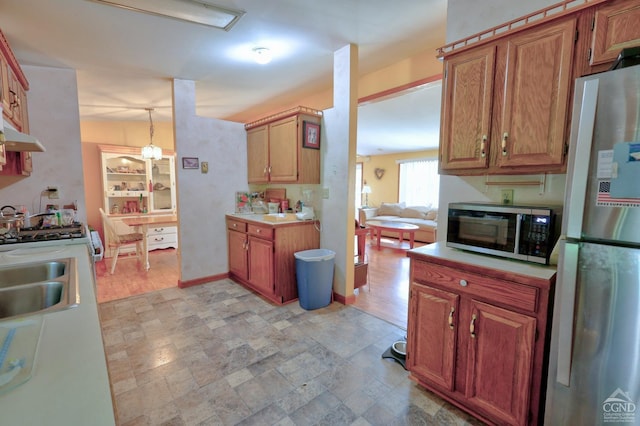 kitchen with baseboards, light countertops, appliances with stainless steel finishes, stone finish floor, and pendant lighting