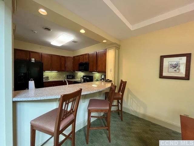 kitchen with a kitchen bar, kitchen peninsula, light stone counters, and black appliances