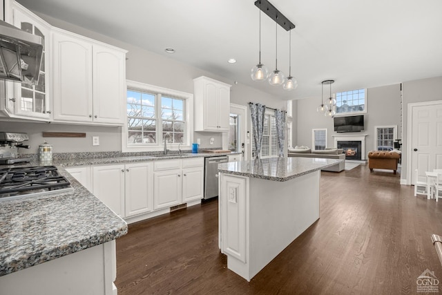 kitchen with a sink, light stone counters, a glass covered fireplace, appliances with stainless steel finishes, and white cabinets