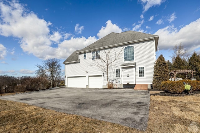 exterior space with aphalt driveway, an attached garage, a pergola, and a shingled roof