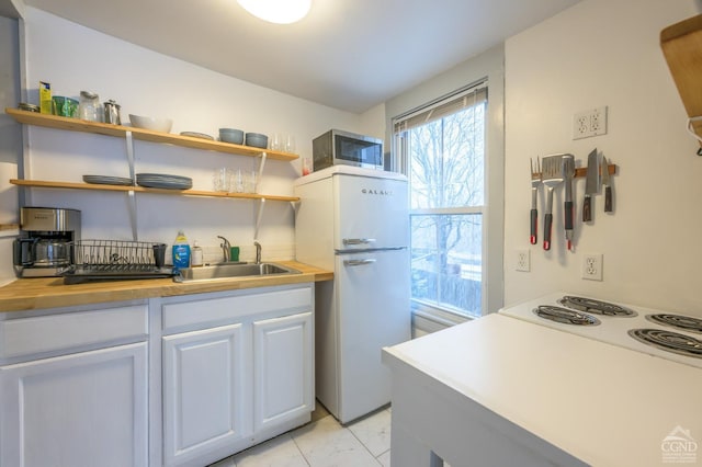 kitchen with stainless steel microwave, a sink, freestanding refrigerator, marble finish floor, and open shelves