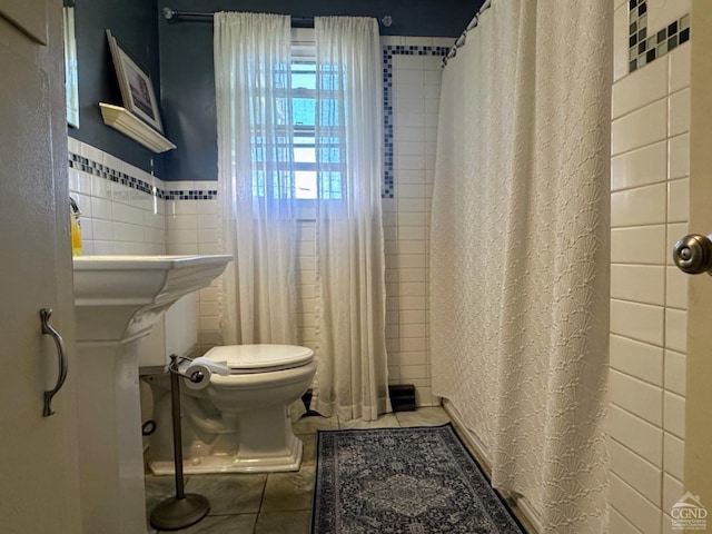 bathroom featuring toilet, a shower with curtain, tile patterned floors, and tile walls