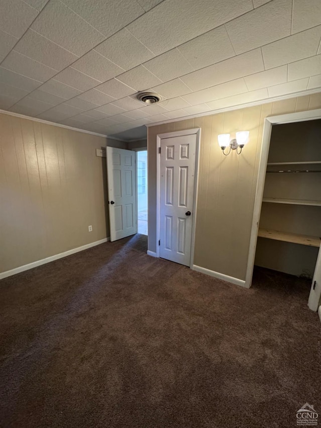 unfurnished bedroom with crown molding, wooden walls, and dark colored carpet