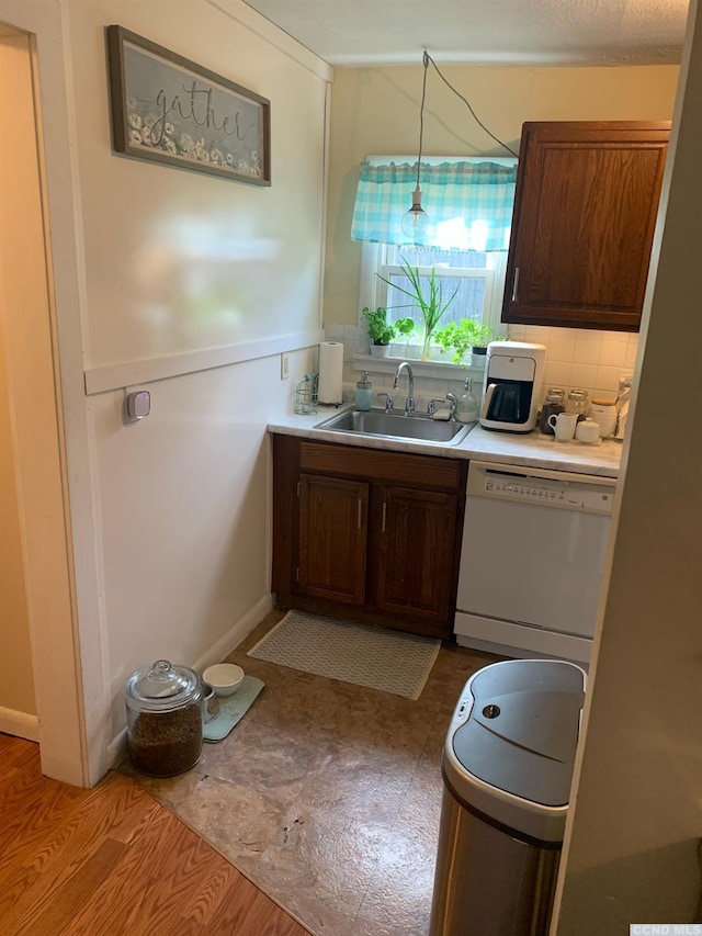 kitchen with tasteful backsplash, white dishwasher, sink, wood-type flooring, and hanging light fixtures