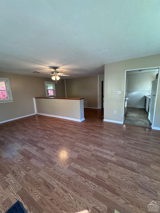 unfurnished room with a textured ceiling, ceiling fan, and dark wood-type flooring