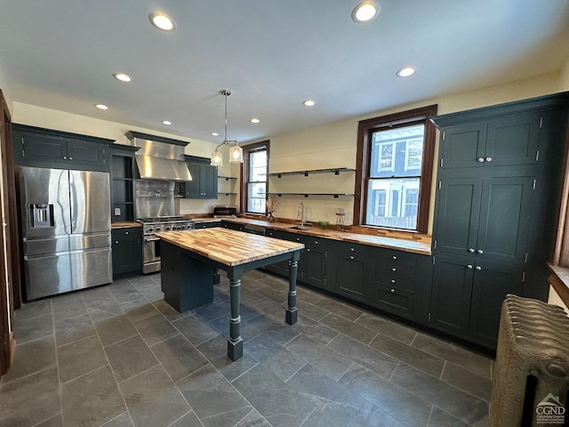 kitchen with sink, butcher block countertops, decorative light fixtures, ventilation hood, and appliances with stainless steel finishes