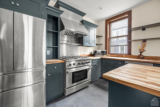 kitchen featuring appliances with stainless steel finishes, range hood, butcher block counters, and dark tile patterned floors