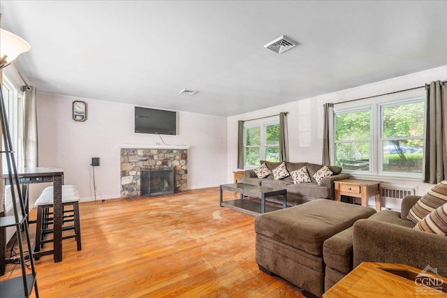 living room with a stone fireplace, radiator, and light wood-type flooring