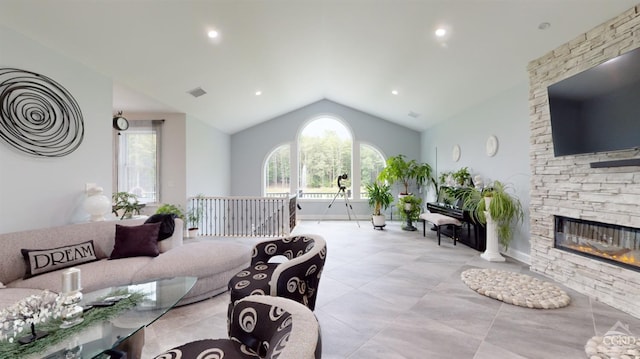 living room with plenty of natural light, a stone fireplace, and vaulted ceiling