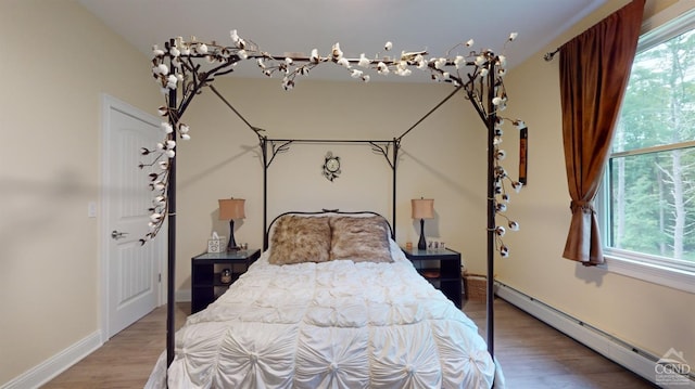 bedroom featuring hardwood / wood-style floors, multiple windows, and a baseboard heating unit