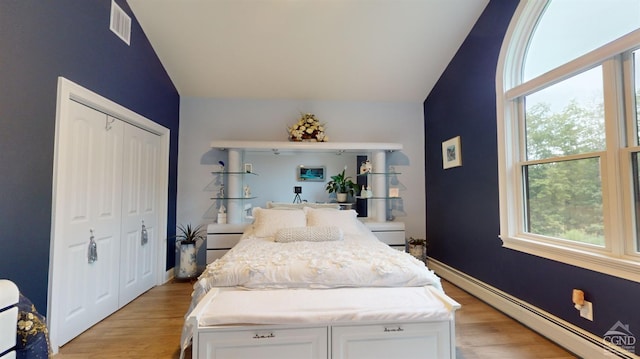 bedroom with a baseboard radiator, vaulted ceiling, a closet, and light hardwood / wood-style floors