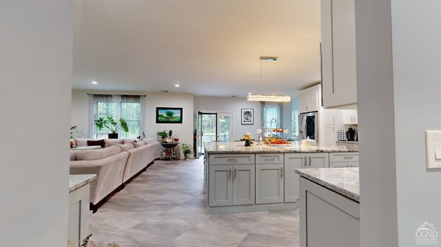 kitchen featuring pendant lighting, light stone countertops, and stainless steel refrigerator