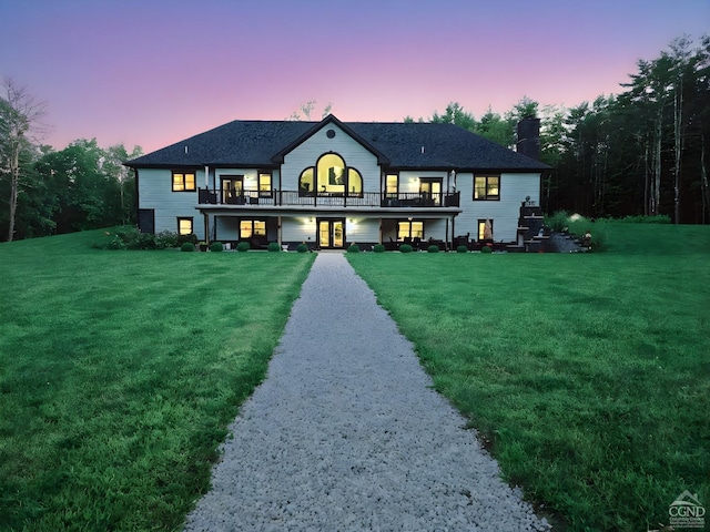 back house at dusk with a balcony and a yard