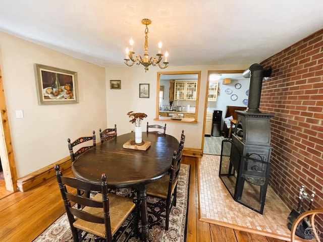 dining area featuring a wood stove, light hardwood / wood-style flooring, a chandelier, and brick wall