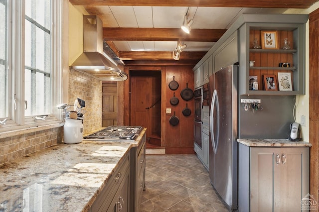 kitchen featuring light stone countertops, appliances with stainless steel finishes, backsplash, and wall chimney range hood