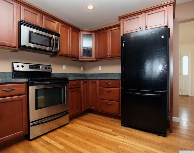 kitchen with dark countertops, light wood-type flooring, appliances with stainless steel finishes, and brown cabinetry